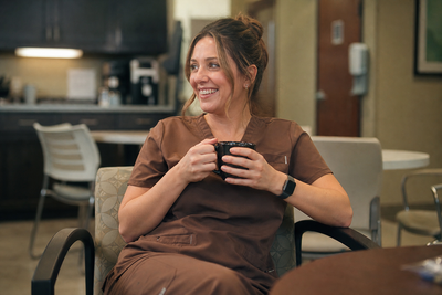 Smiling healthcare worker in coffee-brown scrubs holding a mug during a break